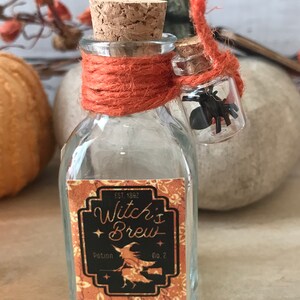 Pu&ograve; includere: Una piccola bottiglia di vetro con un tappo di sughero e un'etichetta che recita "Witch's Brew Potion No. 2". La bottiglia &egrave; legata con uno spago arancione e una piccola fiala di vetro con un ragno nero all'interno &egrave; attaccata allo spago.
