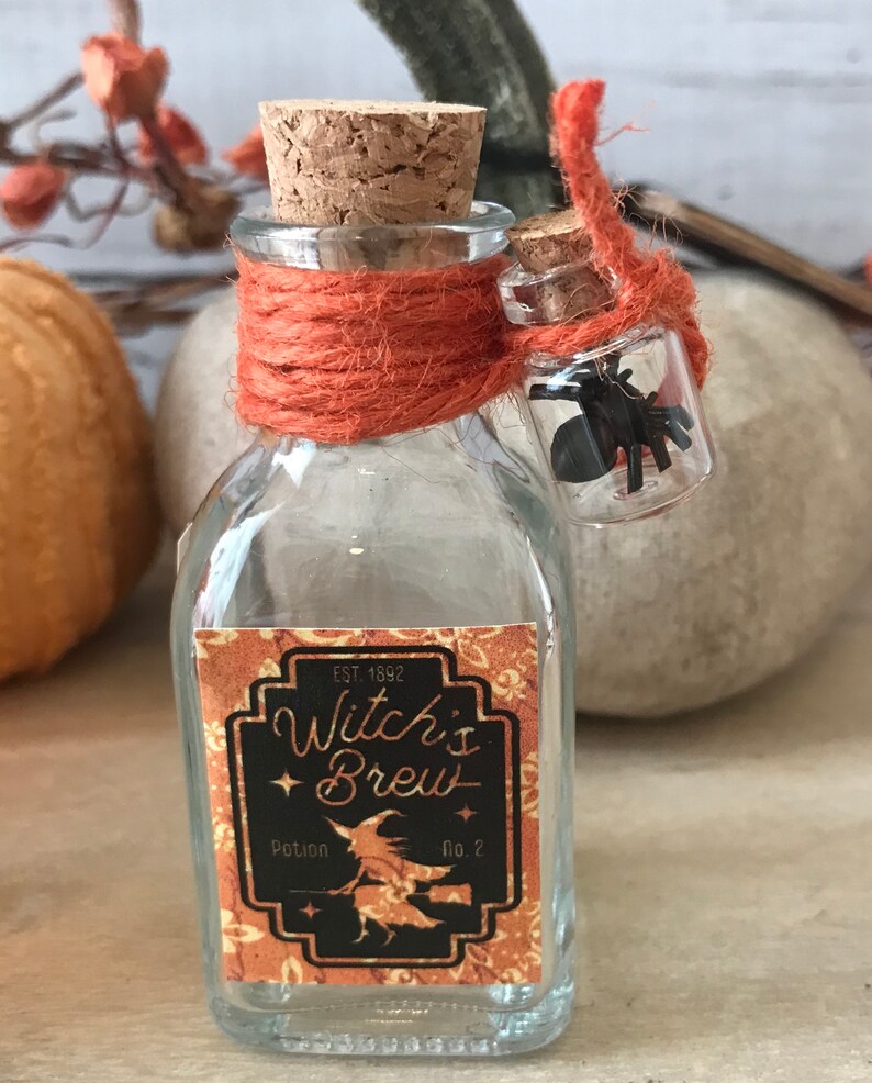 Pu&ograve; includere: Una piccola bottiglia di vetro con un tappo di sughero e un'etichetta che recita "Witch's Brew Potion No. 2". La bottiglia &egrave; legata con uno spago arancione e una piccola fiala di vetro con un ragno nero all'interno &egrave; attaccata allo spago.