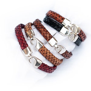 May include: Four braided leather bracelets with silver clasps. The bracelets are stacked on top of each other, with the red bracelet at the bottom and the brown bracelet at the top.