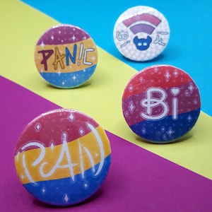 Könnte beinhalten: Vier runde Anstecknadeln mit einem Regenbogenflaggen-Design. Die Knöpfe zeigen die Wörter "PANIC", "BI", "PAN" und ein stilisiertes Symbol einer Person mit einem Regenbogen.