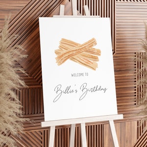 May include: A white sign with a watercolor illustration of churros and the text "Welcome to Billie's Birthday".