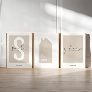 Puede incluir: Tres impresiones artísticas enmarcadas con fondo beige y marcos de madera. Las impresiones presentan diseños minimalistas: una gran letra "S" con la palabra "familie", una silueta de casa y la palabra "zuhause".