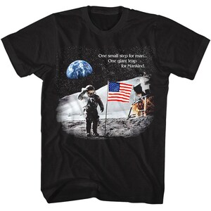 May include: Black t-shirt with a graphic of an astronaut standing on the moon with an American flag planted in the lunar surface. The text "One small step for man... One giant leap for Mankind." is printed on the shirt.