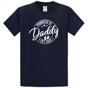 May include: Navy blue t-shirt with a white circle graphic that says "Promoted to Daddy Est. 2025" with a pair of white footprints inside the circle.