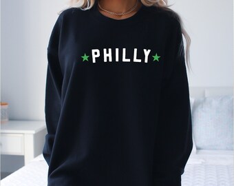 May include: Black sweatshirt with white text that says "PHILLY" with green stars on either side of the text.