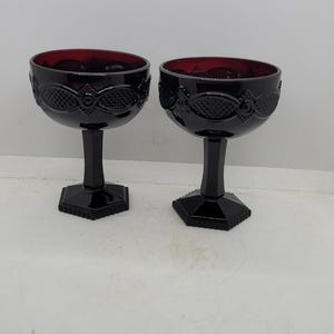 Puede incluir: Dos copas vintage con tallo rojo rubí y negro. Los cuencos son de color rojo intenso, mientras que los tallos y las bases son negros. Las copas tienen un patrón decorativo alrededor del cuenco y una base hexagonal. Ideales para servir cócteles o postres.