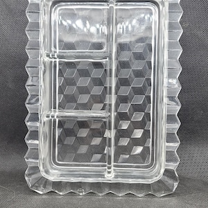 May include: A clear glass serving dish, rectangular with a decorative, scalloped edge. The interior has a geometric cube pattern and is divided into four sections. Ideal for serving snacks.