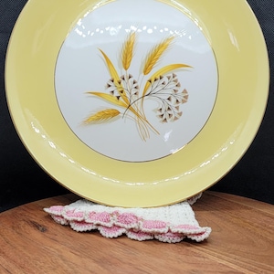 Puede incluir: Un plato de cerámica amarillo con un borde dorado y un centro blanco con un diseño estilizado de espigas de trigo en tonos amarillos y marrones.