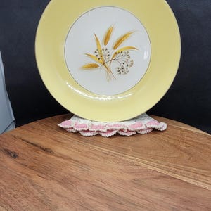 Puede incluir: Un plato de cerámica amarillo con un borde dorado y un centro blanco con un diseño de trigo estilizado.