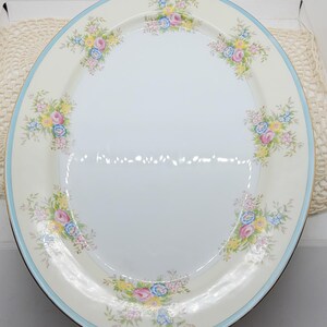Op de afbeelding: Een witte ovale serveerschaal met een blauwe en gouden rand. De schaal is versierd met een bloemenpatroon van roze, gele en blauwe bloemen. De schaal is 41,9 cm lang en 29,8 cm breed.