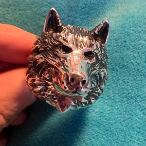 Könnte beinhalten: Ein silberner Wolfskopfring mit einem detaillierten Design. Der Ring ist aus Metall und hat ein realistisches Wolfskopfdesign.