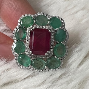 Peut inclure: Une bague en argent ornée d'un grand rubis rectangulaire central, entouré d'émeraudes et de petits diamants. La monture de la bague est détaillée, mettant en valeur les couleurs vives des pierres précieuses.