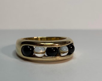May include: A gold-toned ring featuring a series of alternating black and white spherical stones. The ring has a thick band with open spaces that showcase the stones. The design is simple yet elegant, suitable for everyday wear.