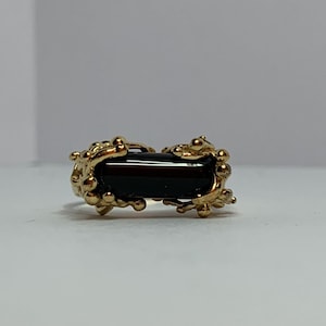 May include: A gold ring featuring a black rectangular stone set within an intricate, organic design.