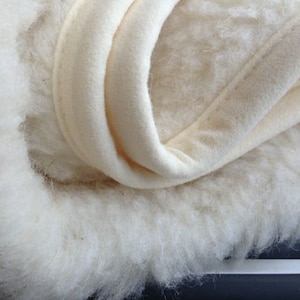 Peut inclure: Gros plan sur un textile cr&egrave;me et duveteux avec une texture douce et moelleuse. Le tissu semble &ecirc;tre superpos&eacute;, avec un bord lisse et pli&eacute;. Le mat&eacute;riau est probablement une couverture ou un article similaire.