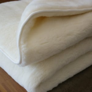 Peut inclure: Une couverture pli&eacute;e, de couleur cr&egrave;me, avec une texture douce et moelleuse. La couverture a une bordure blanche et semble &ecirc;tre faite d'un mat&eacute;riau &eacute;pais et chaud. La couverture est pli&eacute;e proprement, avec une partie de la couche sup&eacute;rieure retourn&eacute;e.