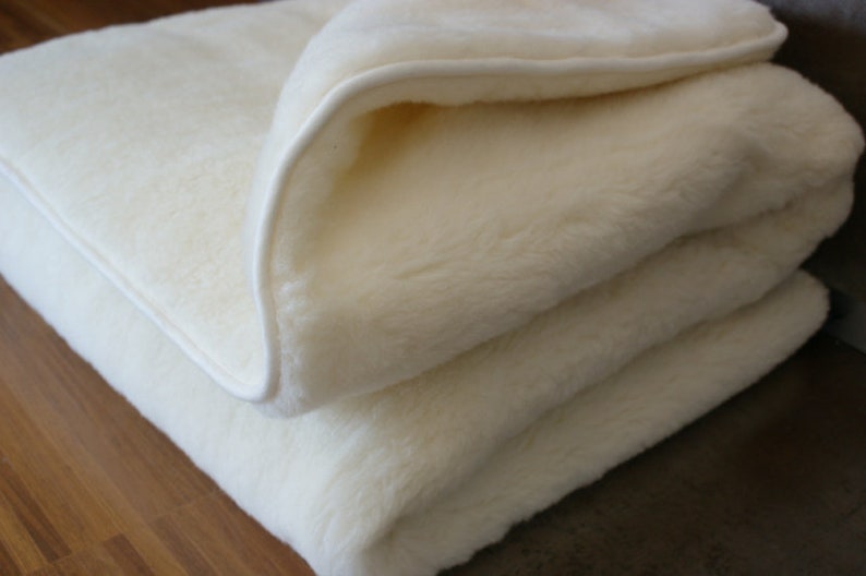 Peut inclure: Une couverture pli&eacute;e, de couleur cr&egrave;me, avec une texture douce et moelleuse. La couverture a une bordure blanche et semble &ecirc;tre faite d'un mat&eacute;riau &eacute;pais et chaud. La couverture est pli&eacute;e proprement, avec une partie de la couche sup&eacute;rieure retourn&eacute;e.