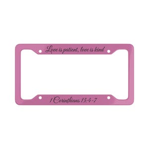 May include: A pink license plate frame with the text "Love is patient, love is kind" and "1 Corinthians 13:4-7" in black script. The frame has a rectangular shape with rounded corners and pre-drilled holes for mounting.