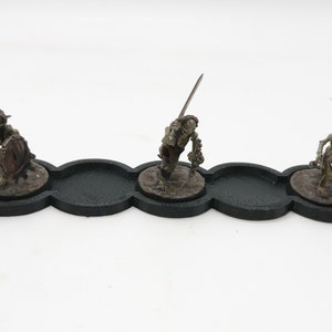May include: Three miniature skeletal figures with swords and shields are displayed on a black plastic base with three circular indentations.