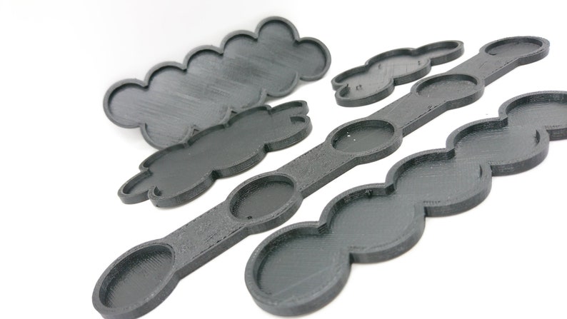 May include: Four black plastic paint palettes with different shapes and sizes. The palettes have circular wells for holding paint.