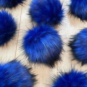 May include: Multiple blue faux fur pom poms with black tips. The pom poms are arranged in a row on a light wood surface.