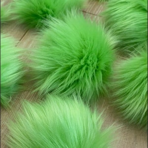 May include: A collection of six fluffy green pom-poms. The pom-poms are made of soft, plush fur and are perfect for adding a touch of whimsy to any project.