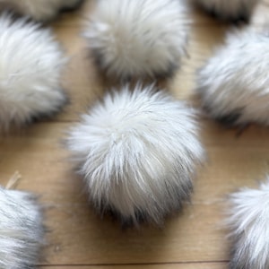 May include: A group of white and black faux fur pom poms. The pom poms are soft and fluffy and would be great for adding a touch of whimsy to any project.