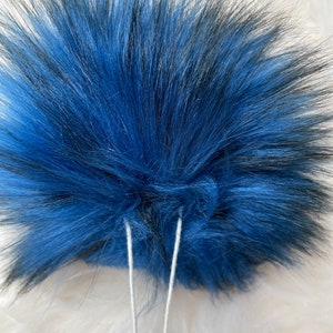 Peut inclure: Un pompon en fausse fourrure bleu et noir avec deux cordons blancs attach&eacute;s.