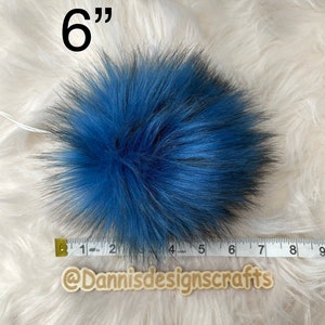 Peut inclure: Un pompon en fausse fourrure bleu et noir de 15 cm de diam&egrave;tre. Le pompon est pr&eacute;sent&eacute; sur une surface moelleuse blanche avec un ruban de mesure.