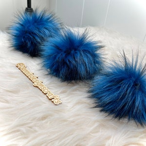 Peut inclure: Trois pompons en fausse fourrure bleue sur une surface blanche et moelleuse. Les pompons sont doux et moelleux, et ils seraient parfaits pour ajouter une touche de fantaisie &agrave; n'importe quel projet.