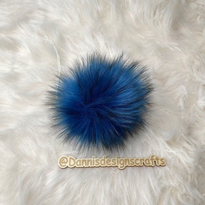 Peut inclure: Un pompon bleu moelleux avec une ficelle blanche attach&eacute;e. Le pompon est sur une surface moelleuse blanche.