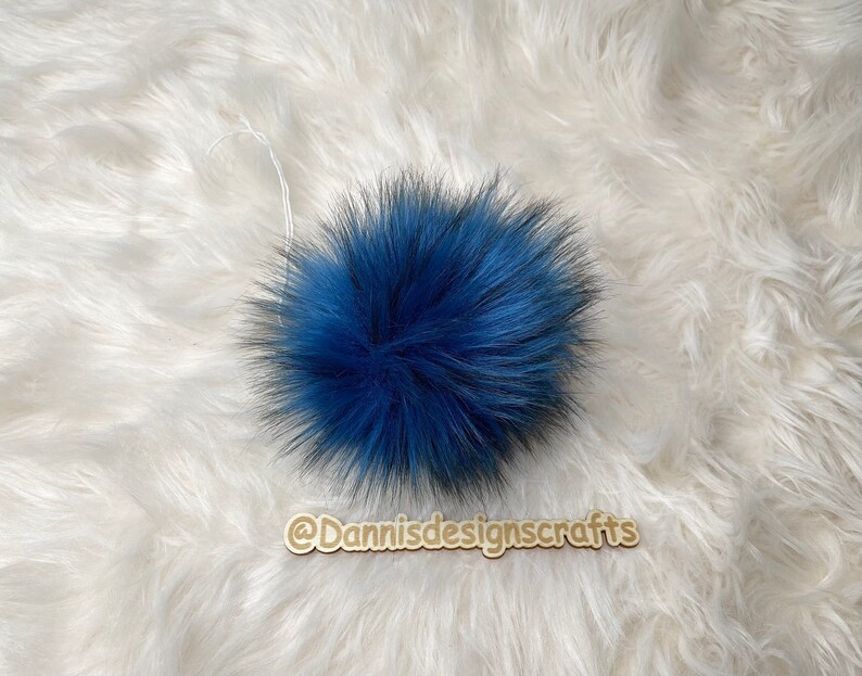 Peut inclure: Un pompon bleu moelleux avec une ficelle blanche attach&eacute;e. Le pompon est sur une surface moelleuse blanche.