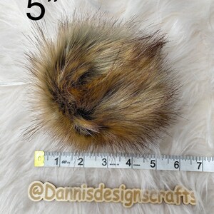 May include: A 5 inch brown and gray faux fur pom pom. The pom pom is measured with a white tape measure.