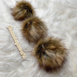 May include: Three brown faux fur pom poms on a white fluffy surface.