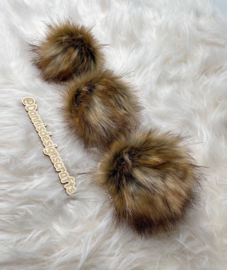 May include: Three brown faux fur pom poms on a white fluffy surface.