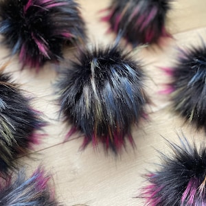 May include: A collection of six fluffy pom poms in various shades of black, blue, pink, and green. The pom poms are made of faux fur and have a soft, textured appearance.