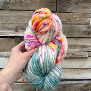 May include: A large skein of colorful yarn in shades of pink, yellow, and teal. The yarn is thick and chunky, with a soft, textured appearance. The colors are vibrant and create a visually appealing effect, perfect for knitting or crocheting projects.