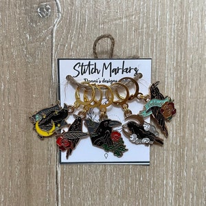 May include: Set of six gold stitch markers with black crow and moon designs. The markers are on a white card with the text "Stitch Markers" and "Danni's designs".