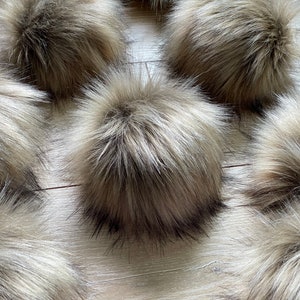 May include: Six fluffy brown and black faux fur pom poms on a light wood surface.