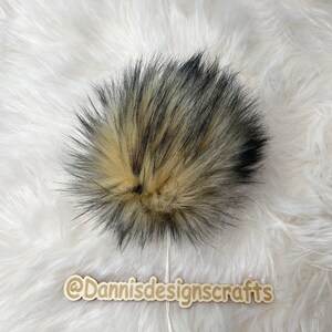 May include: A fluffy black and beige faux fur pom pom. The pom pom is about 5 inches in diameter and is perfect for adding a touch of whimsy to hats, scarves, or other accessories.