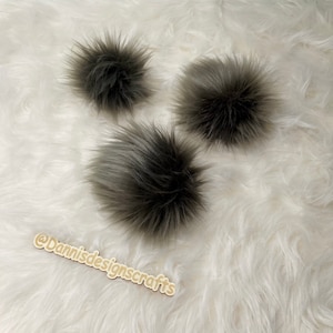 May include: Three gray faux fur pom poms on a white fluffy surface.