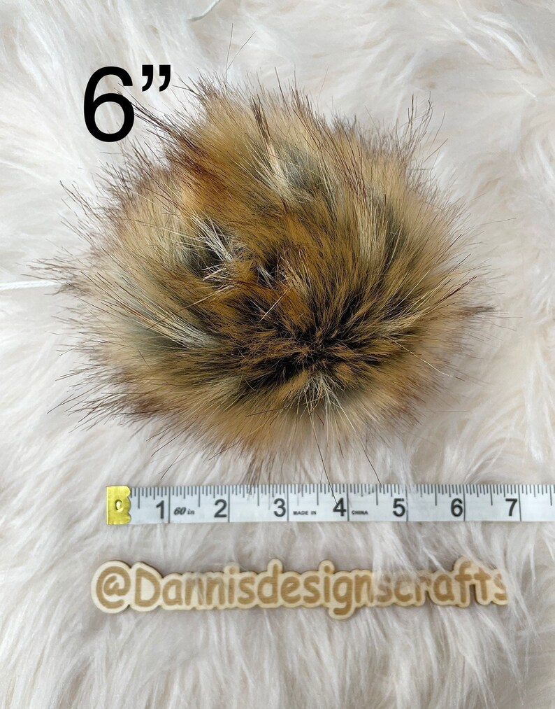 May include: A 6 inch faux fur pom pom in brown, black, and white colors. The pom pom is measured with a tape measure.