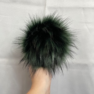 May include: A dark green faux fur pom pom. The pom pom is fluffy and has a soft texture.