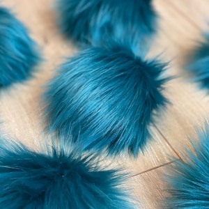 May include: A close-up of several teal blue fluffy pom poms. The pom poms are soft and plush, and they would be perfect for adding a touch of whimsy to any project.