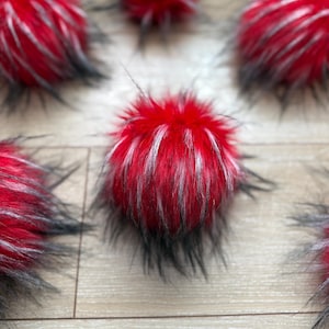 Puede incluir: Una colección de pompones rojos y negros peludos. Los pompones están hechos de un material suave y esponjoso y tienen un patrón a rayas.