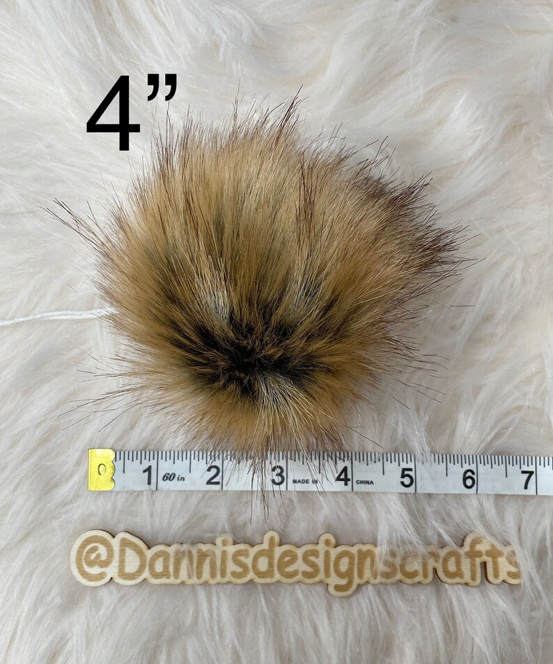 May include: A 4 inch brown and black faux fur pom pom. The pom pom is measured with a tape measure.