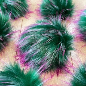 May include: Multiple green faux fur pom poms with white and pink highlights. The pom poms are soft and fluffy.