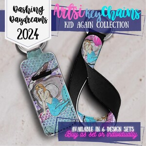 May include: A colorful mermaid keychain with a blue tail and pink seashell. The keychain is made of fabric and has a black strap. The text "Bashing Daydreams 2024" and "Artsi Key Chains Kid Again Collection" is visible in the background.