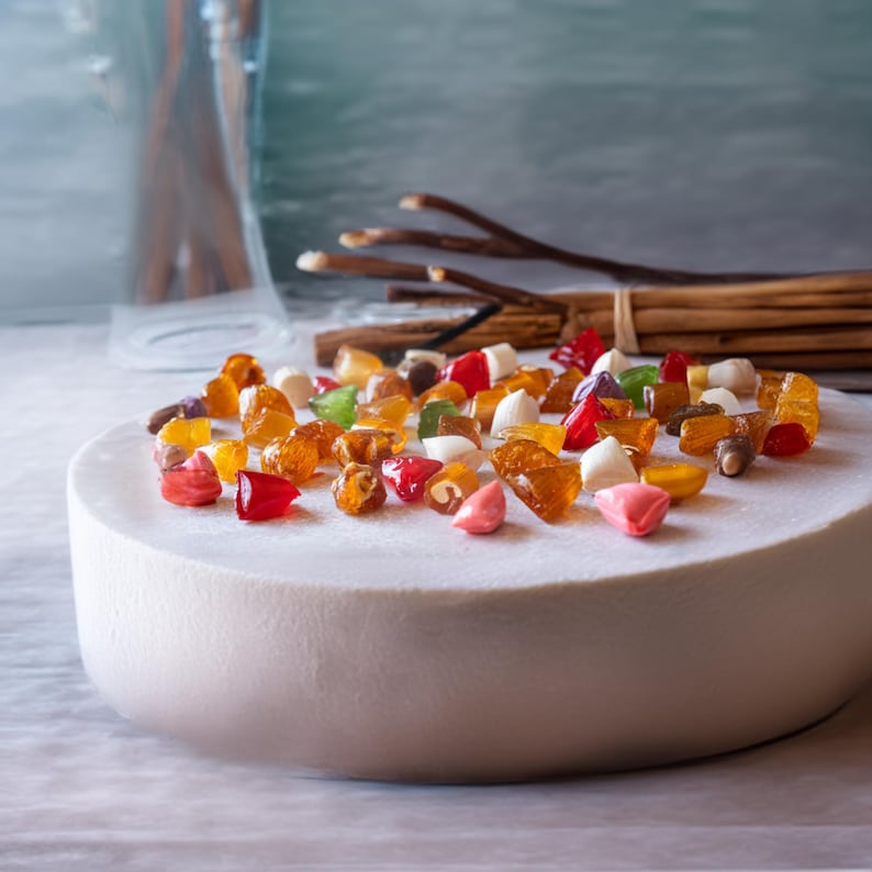 May include: A white cake with a variety of colorful candies on top. The candies are in different shapes and sizes, and some are translucent. The cake is on a white surface.