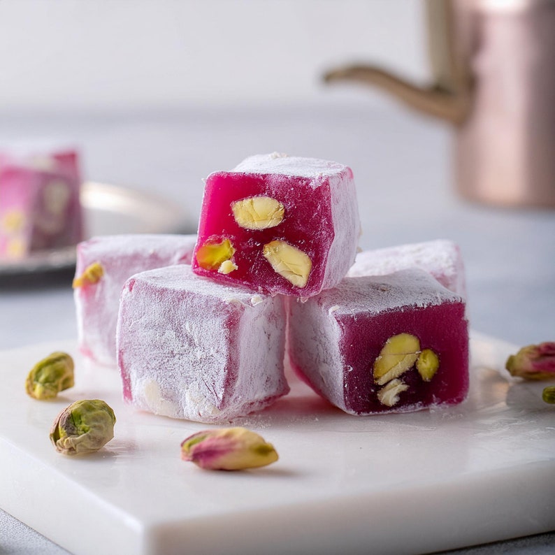 K&ouml;nnte beinhalten: Rosa t&uuml;rkische S&uuml;&szlig;warenw&uuml;rfel mit Pistazien, mit Puderzucker best&auml;ubt, auf einer wei&szlig;en Oberfl&auml;che.